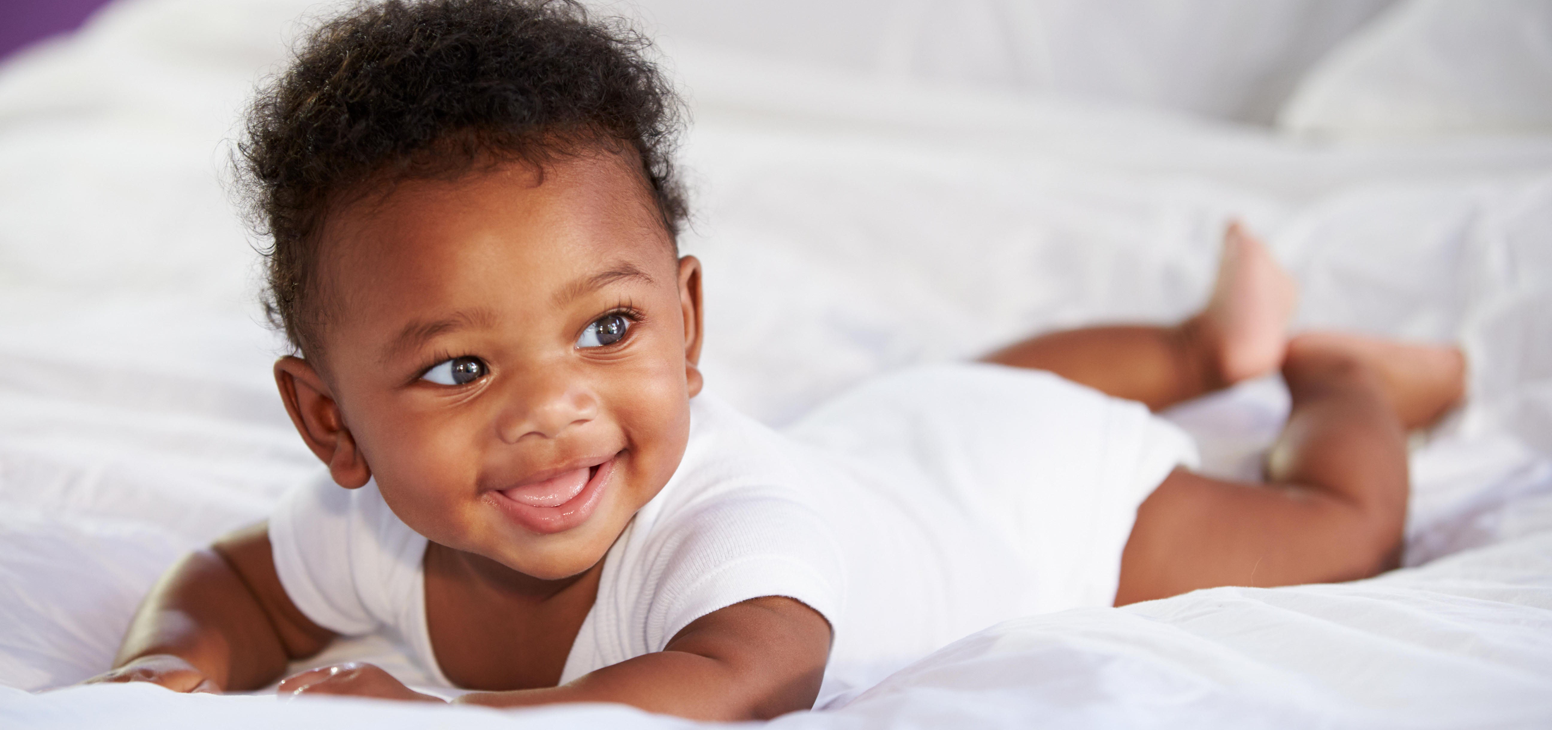Bebé sonriendo acostado en la cama boca abajo
