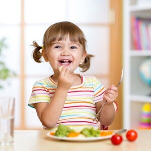 Pequeña comiendo verduras durante la comida.