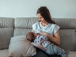 Mamá sentada en un sofá sonriendo, amamantando a su bebé. Lactancia materna.
