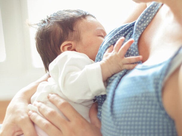 Mamá en etapa de posparto, sosteniendo por el pecho a su bebé recién nacido.