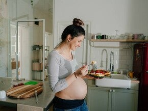 Mujer embarazada sonriendo en la cocina comiendo antojo dulce