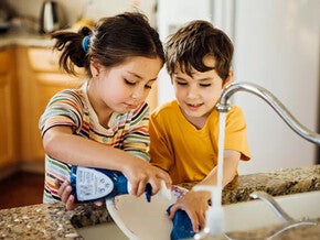 Niña y niño lavando un plato en la cocina.