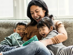 Madre y dos niños pequeños sentados en un sofá, leyendo un cuento, sonriendo.