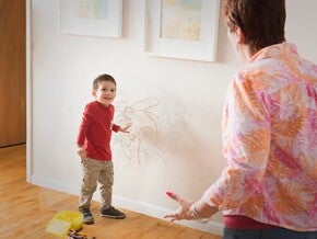 Niño con dibujos de crayón por la pared y un adulto reaccionando.