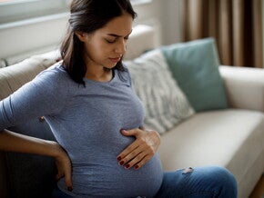 Conoce qué es la eclampsia y cuáles son sus causas.  Mamá tocando el vientre y la espalda sintiendo molestia.