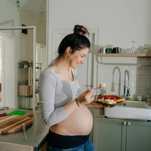 Mujer embarazada sonriendo en la cocina comiendo antojo dulce