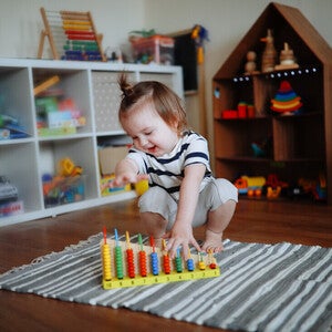 Niña de dos años jugando sobre la alfombra con ábaco de madera. Juego tranquilo como rutina diaria.