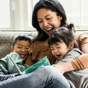 Madre y dos niños pequeños sentados en un sofá, leyendo un cuento, sonriendo.