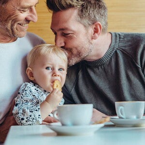 Conoce cuándo puedes darle galletas para bebés a tu hijo. Niña comiendo galletas para bebés con su papá y abuelo.