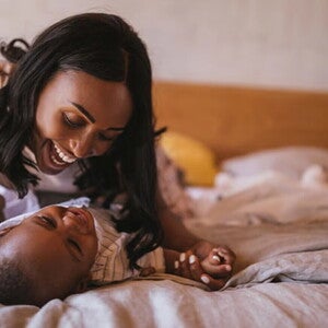 Estimulación temprana para bebés Mamá haciendo ejercicios de estimulación temprana con su bebé en la cama, mientras los dos sonríen.