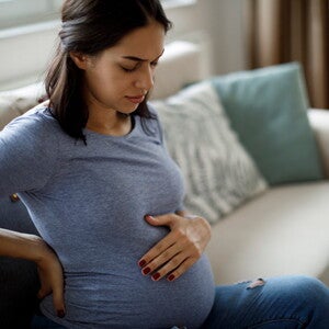 Conoce qué es la eclampsia y cuáles son sus causas. Mamá tocando el vientre y la espalda sintiendo molestia.