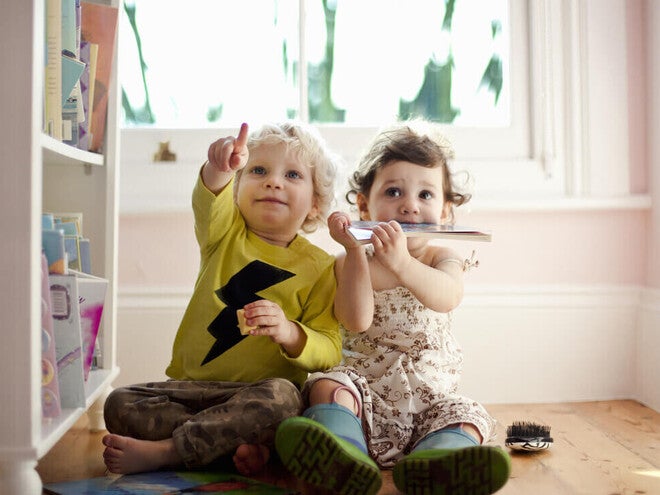 Niño y niña de dos años sentados en el piso, señalando. Concepto de comunicación y desarrollo de lenguaje.