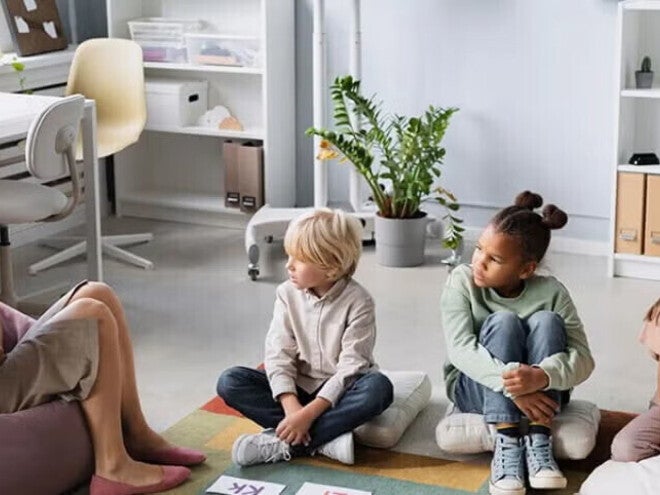 Patólogo del habla y lenguaje, SLP terapeuta del habla y lenguaje, fonoaudiólogo mostrando abecedario a niños pequeños sentados sobre cojines.