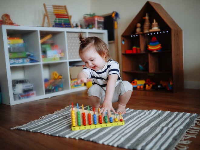 Niña de dos años jugando sobre la alfombra con ábaco de madera. Juego tranquilo como rutina diaria.