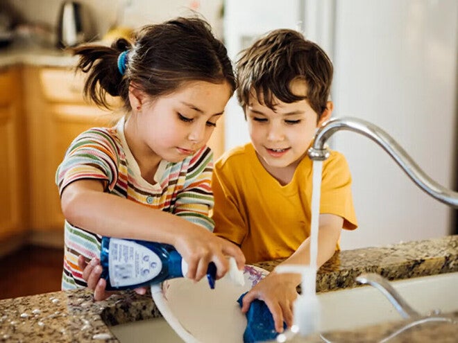 Niña y niño lavando un plato en la cocina.