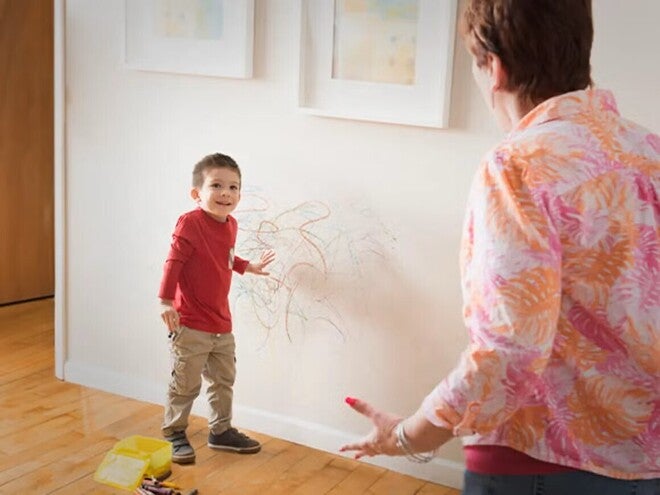 Niño con dibujos de crayón por la pared y un adulto reaccionando.