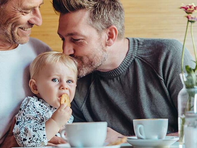 Conoce cuándo puedes darle galletas para bebés a tu hijo. Niña comiendo galletas para bebés con su papá y abuelo.