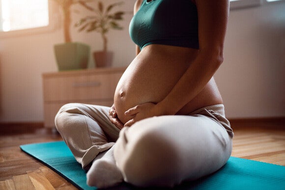 Mujer embarazada sentada con las rodillas cruzadas en una colchoneta de yoga.