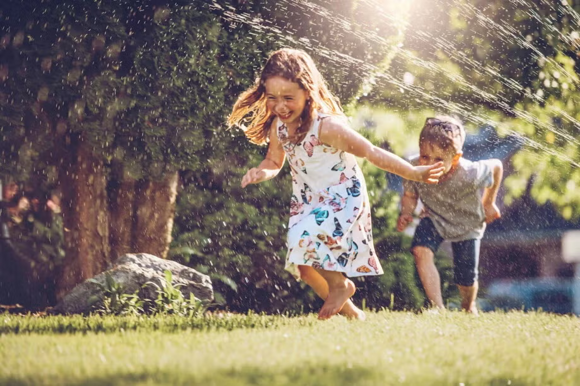 Niños jugando en el pasto con el rociador, llenos de energía por comer alimentos energéticos.