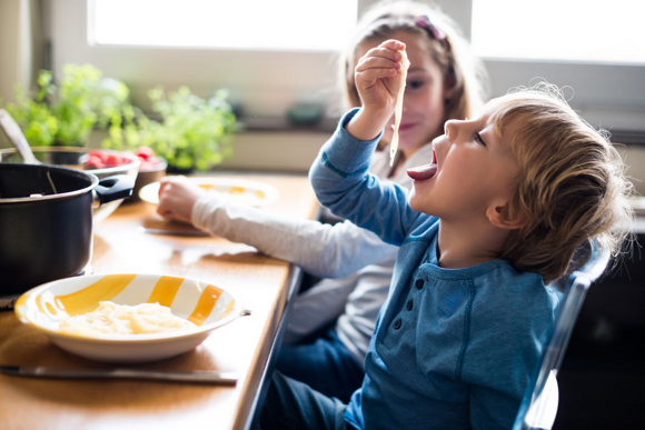 Niño pequeño sentado en frente a la mesa comiendo pasta con las manos, uno de los alimentos energéticos para niños.