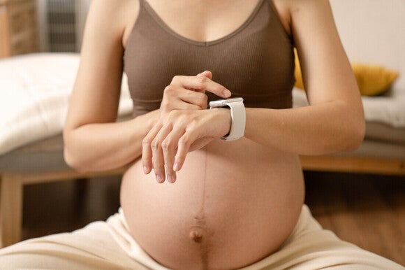 Mujer embarazada sentada en una colchoneta de ejercicios y cronometrando contracciones.