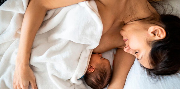 El primer mes, la leche materna pasa por muchos procesos, desde el calostro hasta la leche madura que será la definitiva y el alimento para tu bebé. Mamá acostada alimentando a su bebé recién nacido.