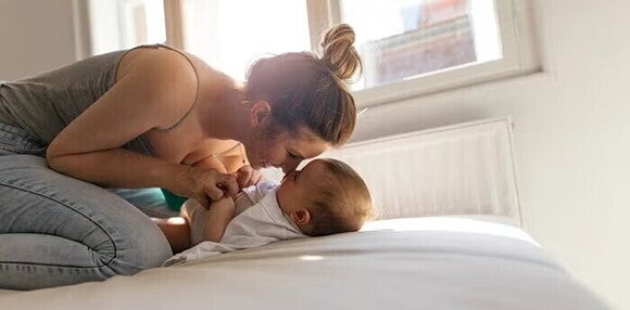 Gimnasia para bebés Mamá haciendo ejercicios de gimnasia para bebés con su bebé en la cama, mientras los dos sonríen.