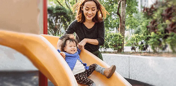 Visitar el parque es excelente para el desarrollo de habilidades motrices. Mamá ayudando a hija pequeña a bajar de un tobogán en el parque.