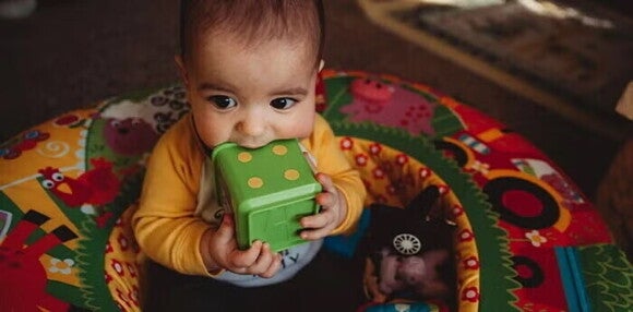 Las manos y boca son las principales herramientas para explorar Bebé sujetando un cubo de juguete con sus manos.